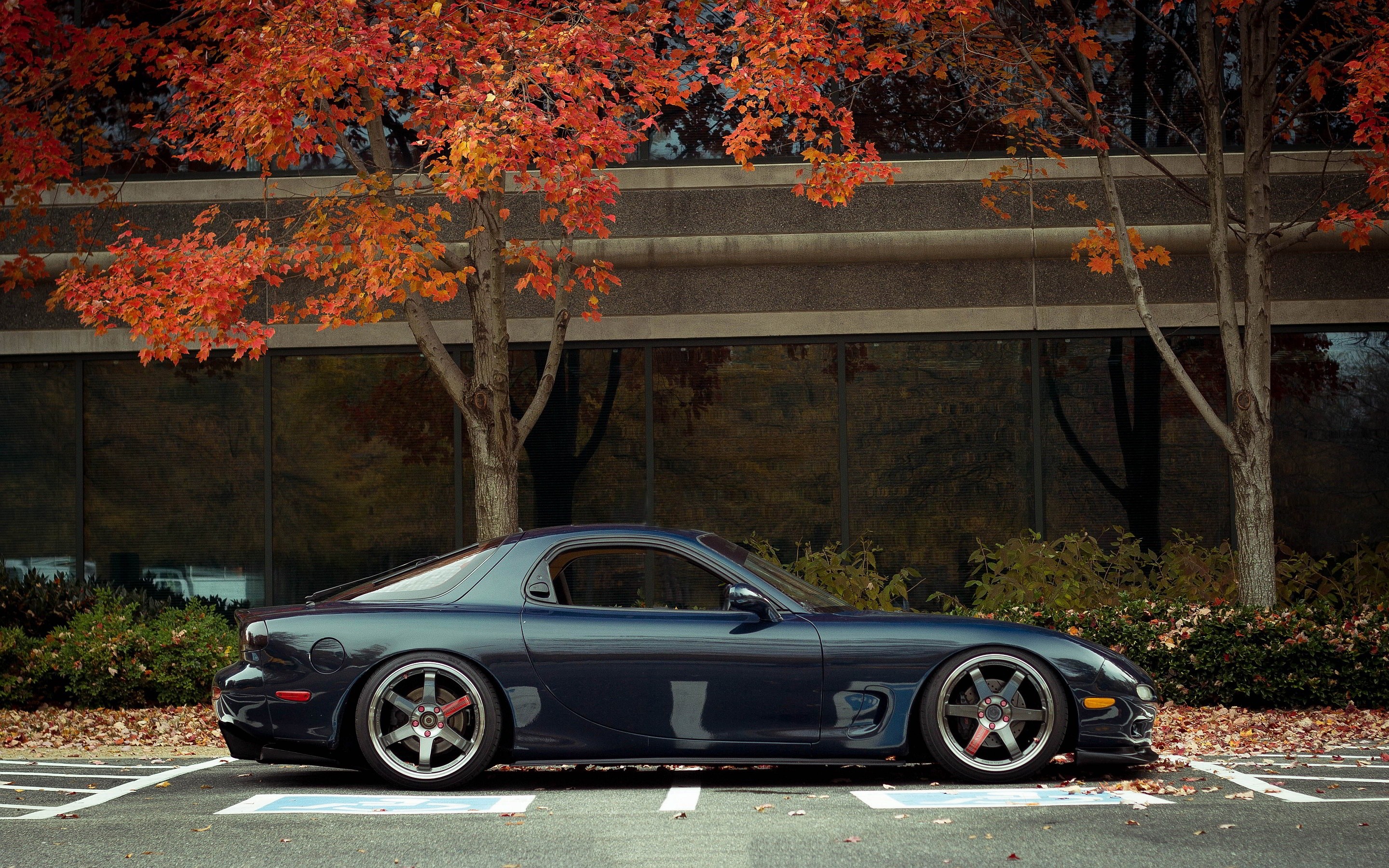 Mazda RX-7 parked in front of a building with autumn trees HD Wallpaper