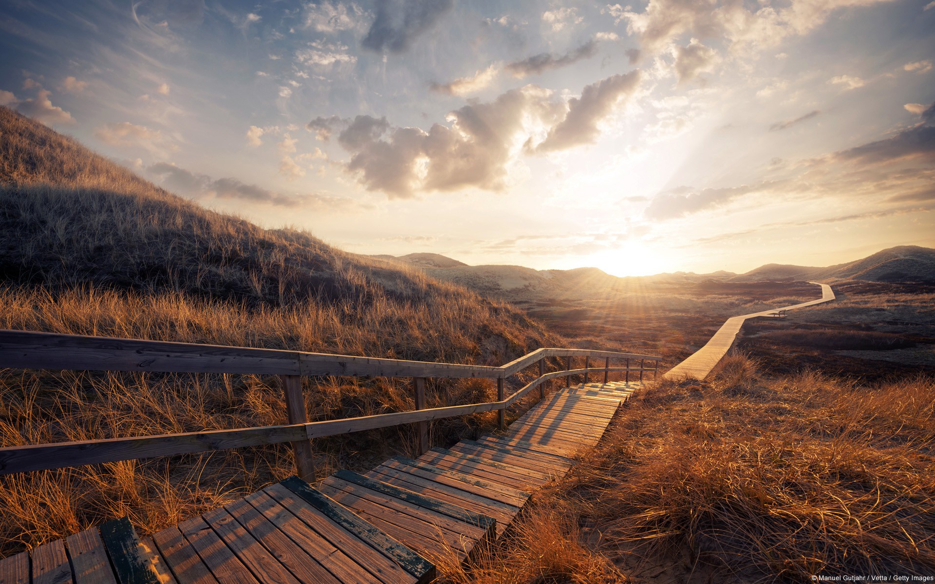 Wooden boardwalk through grassy dunes at sunset HD Wallpaper