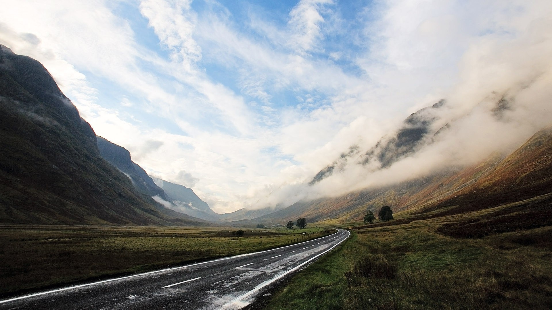 A scenic road winds through a misty mountain valley HD Wallpaper