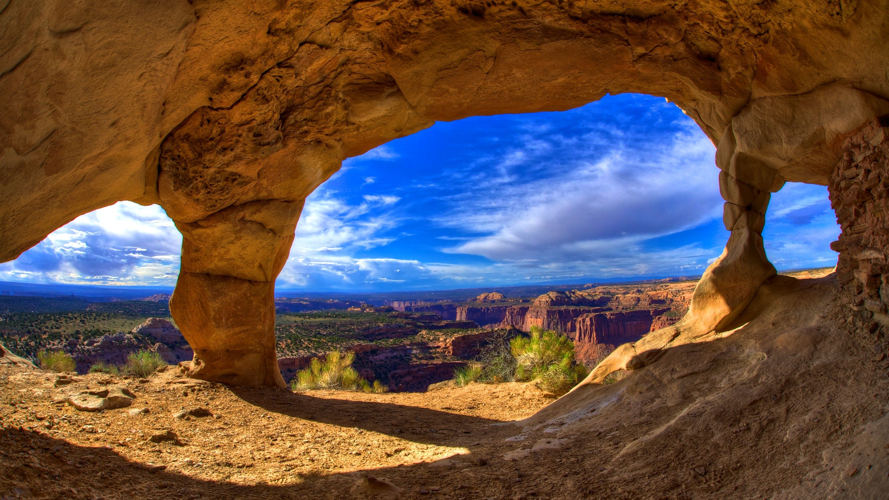 Cave opening overlooking a vast canyon landscape HD Wallpaper