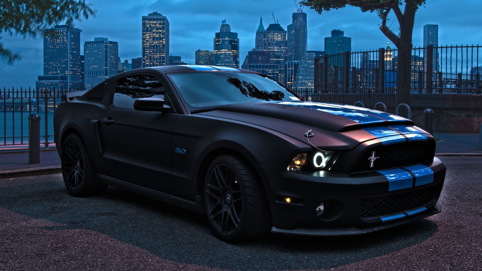 Matte black Ford Mustang with blue stripes in city HD Wallpaper
