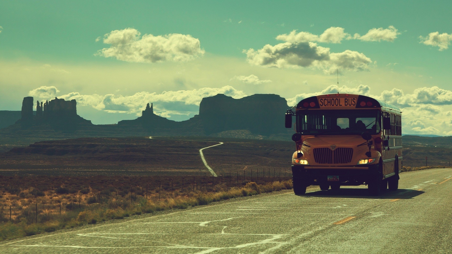 Yellow school bus driving on a road in Monument Valley HD Wallpaper