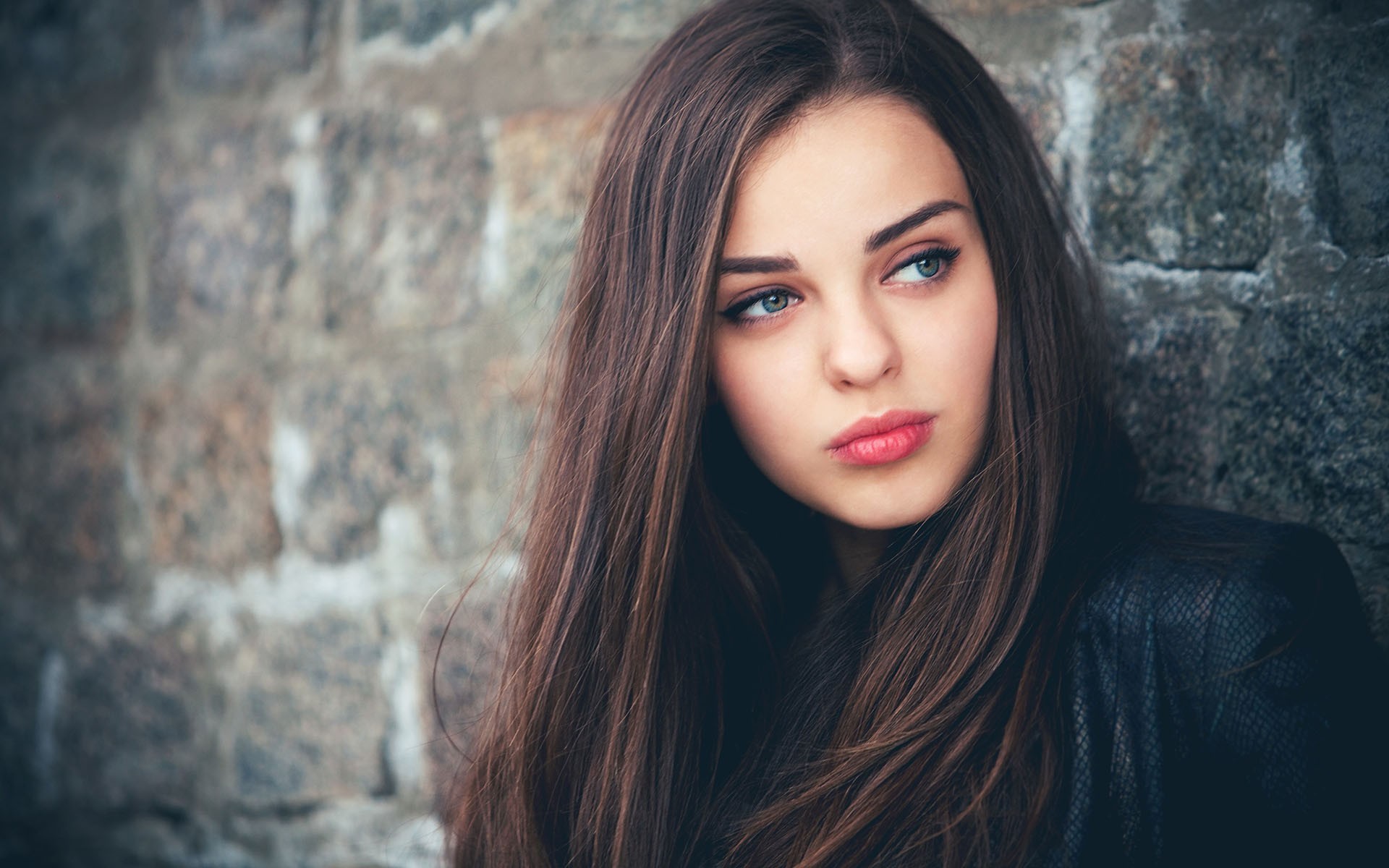 Woman with long brown hair leaning against a stone wall HD Wallpaper