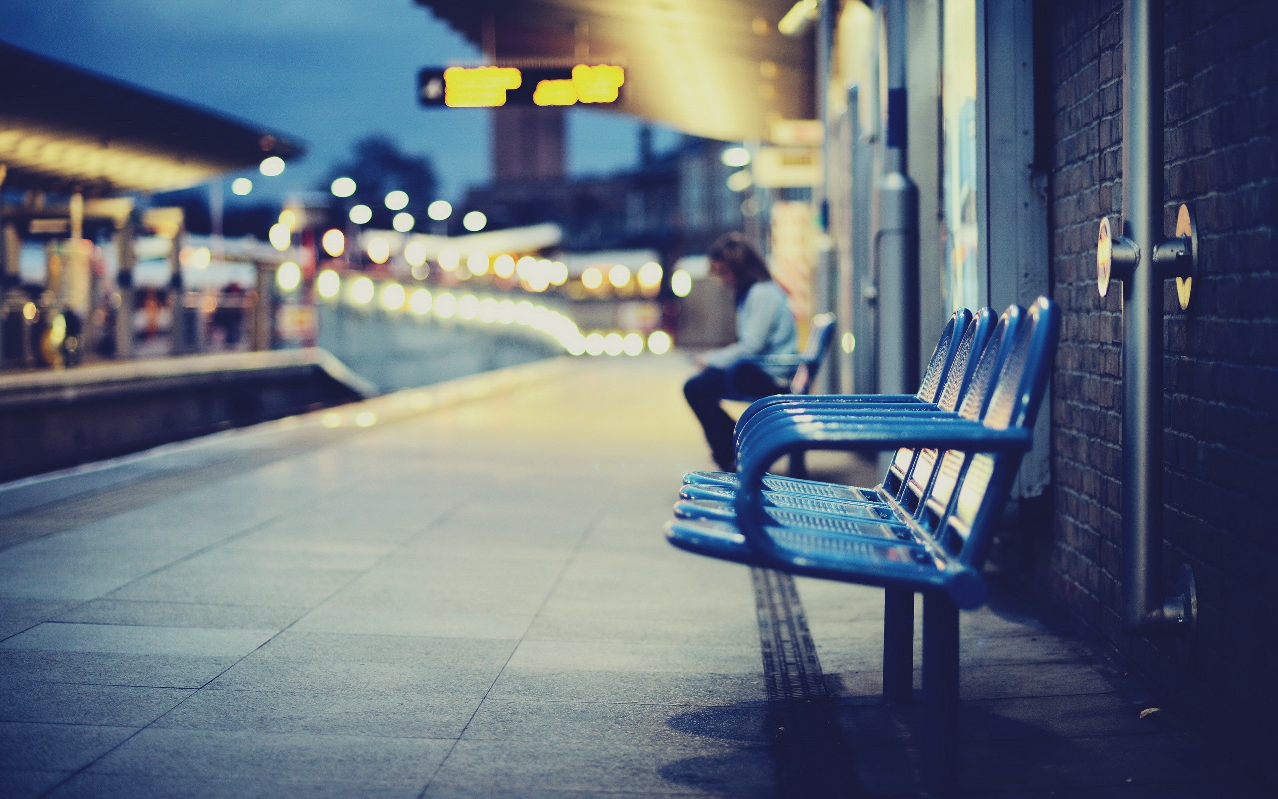 Person sitting on a bench at a railway station at night HD Wallpaper