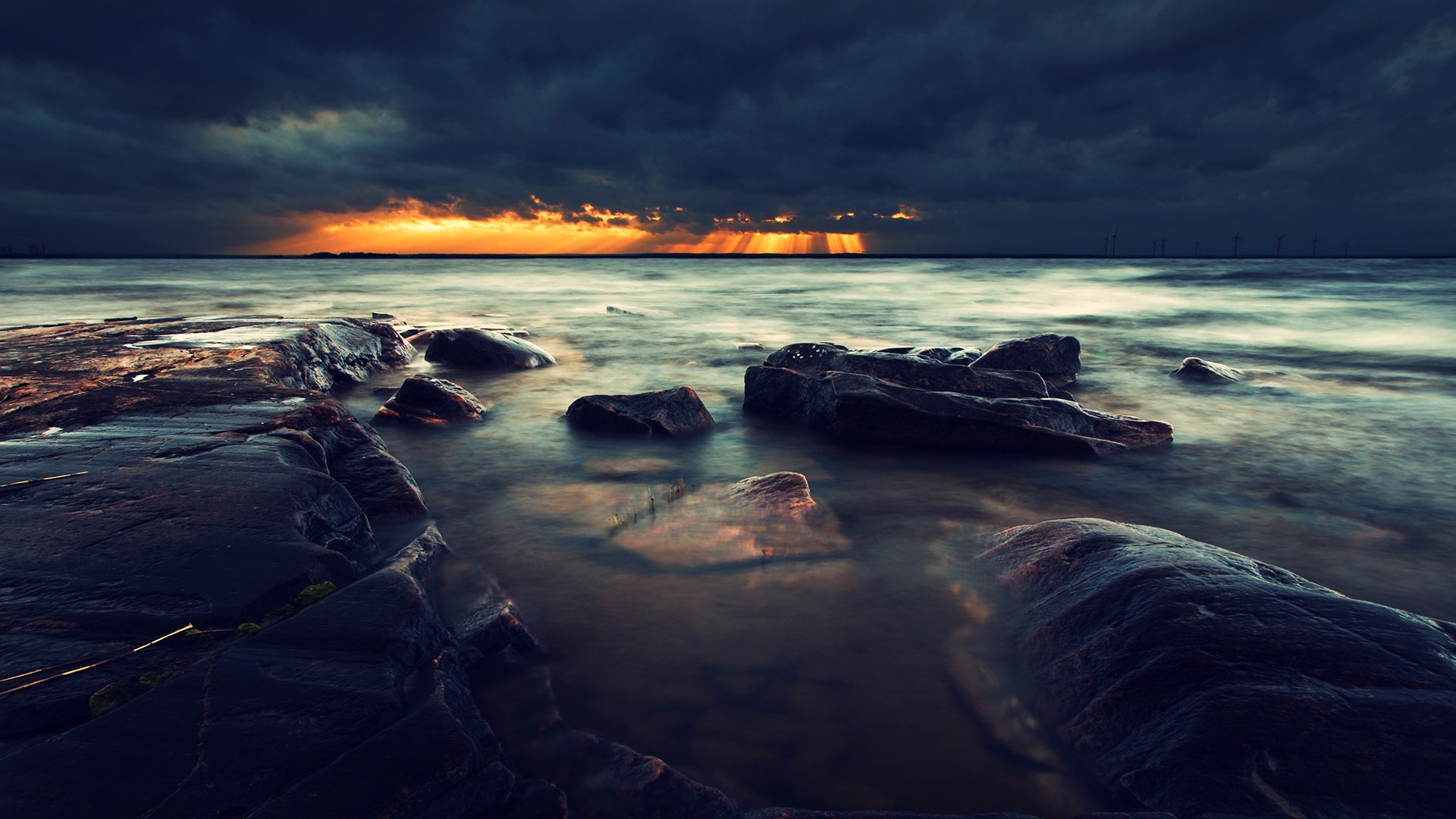 Stormy sea with sunbeams over rocky shore HD Wallpaper