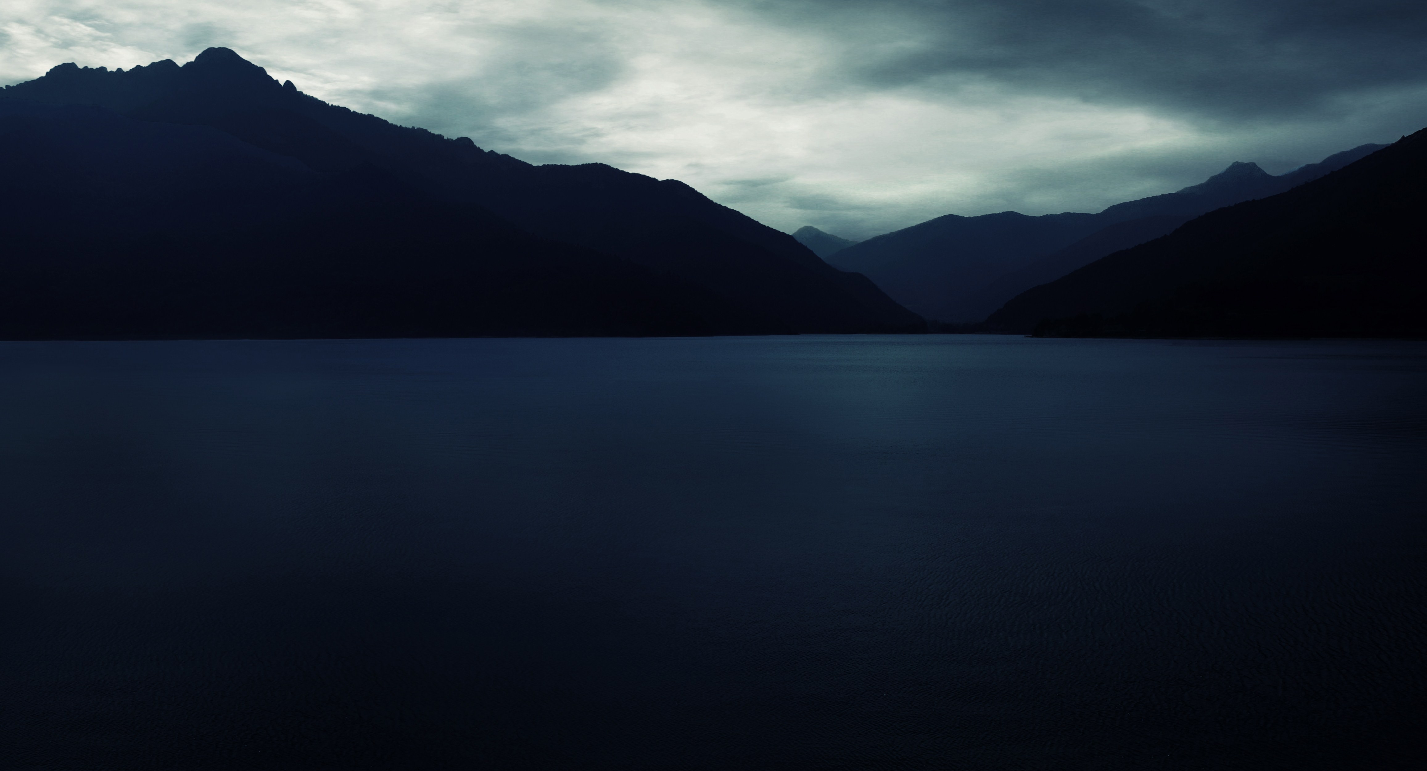 Dark mountains over a calm lake under a cloudy sky HD Wallpaper