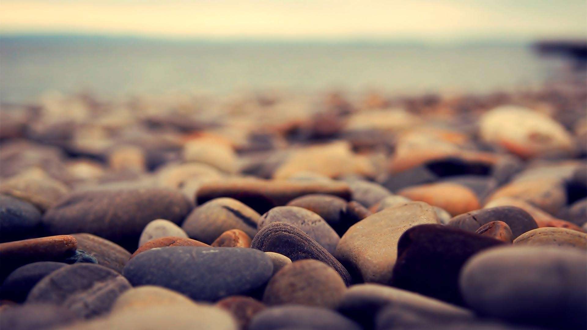 Close-up of smooth stones on a beach with the ocean in the background HD Wallpaper