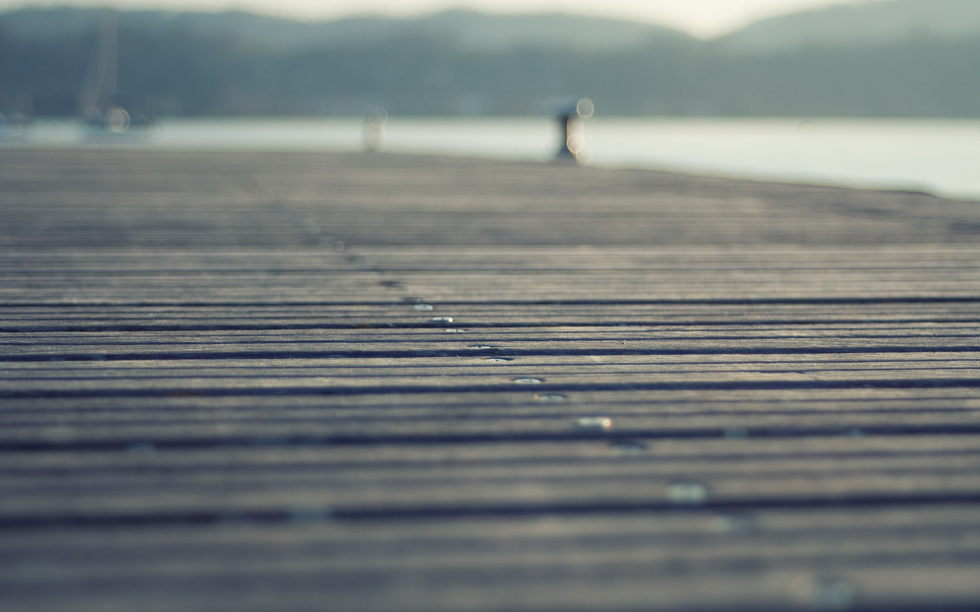 Wooden pier extending over water with hills in background HD Wallpaper
