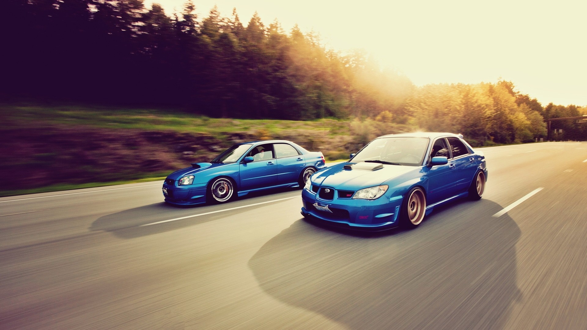 Two blue Subaru Imprezas driving on a road HD Wallpaper