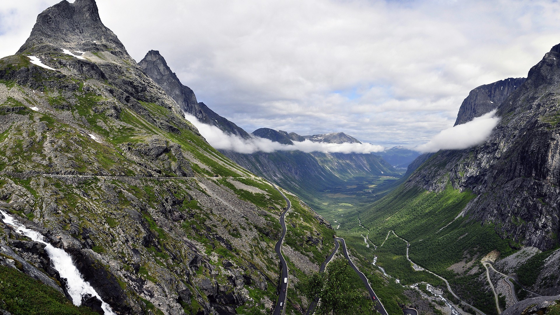 Winding road through a green mountain valley with clouds HD Wallpaper