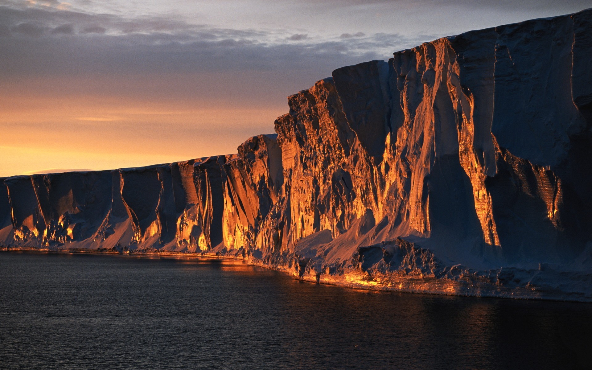 Iceberg cliff illuminated by sunset over the sea HD Wallpaper