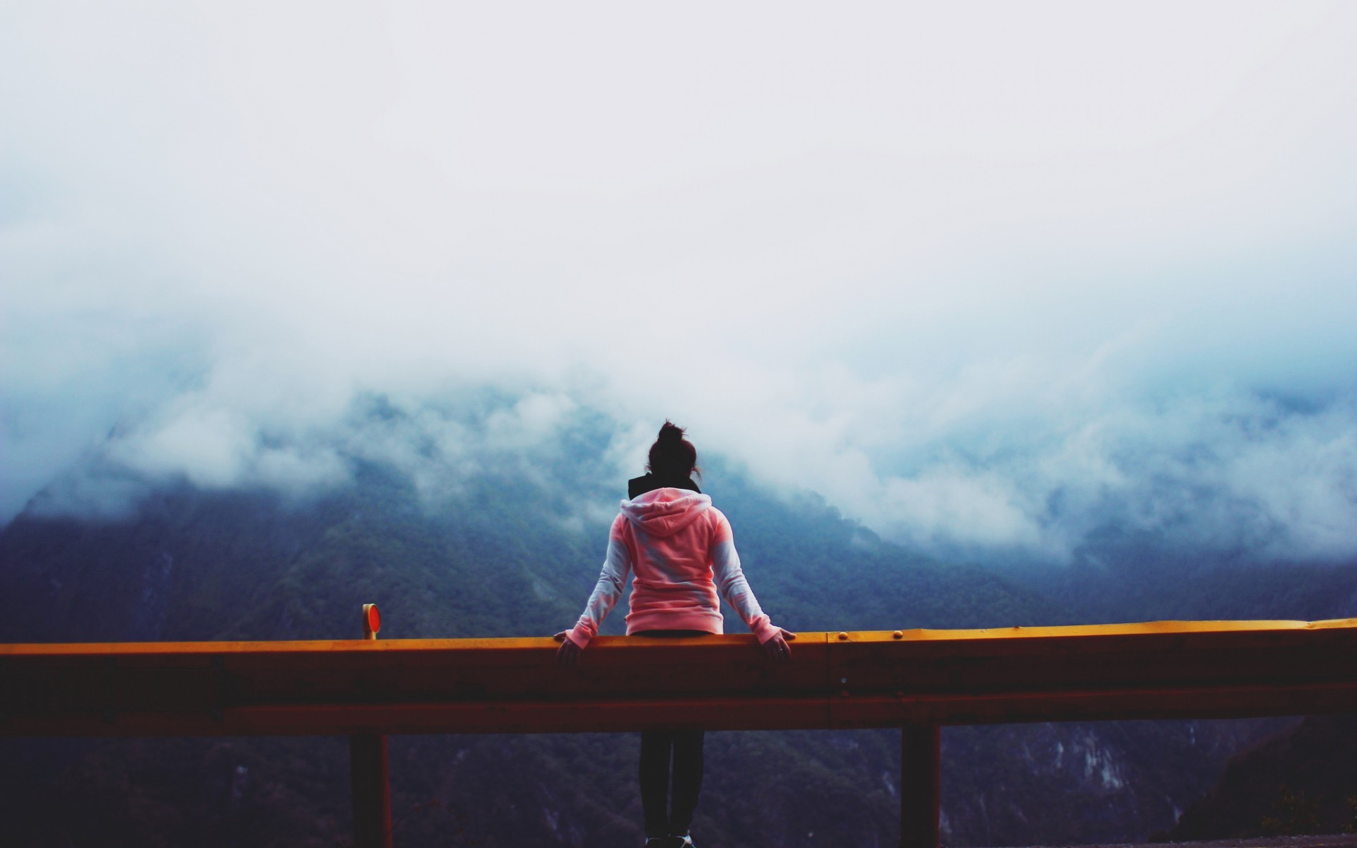 Woman sitting on a guardrail overlooking mountains HD Wallpaper