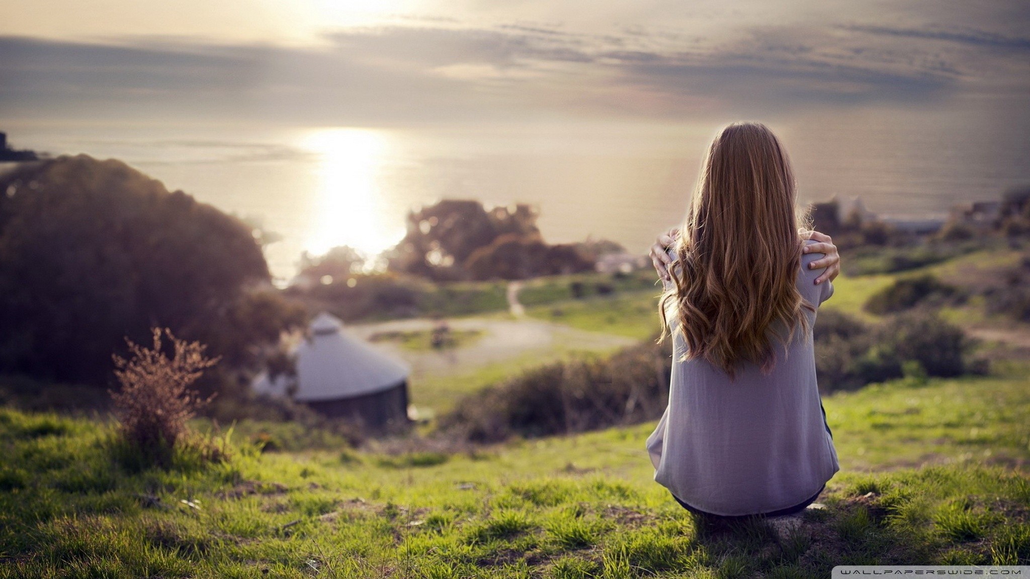 Woman with long hair sitting outdoors overlooking the ocean HD Wallpaper