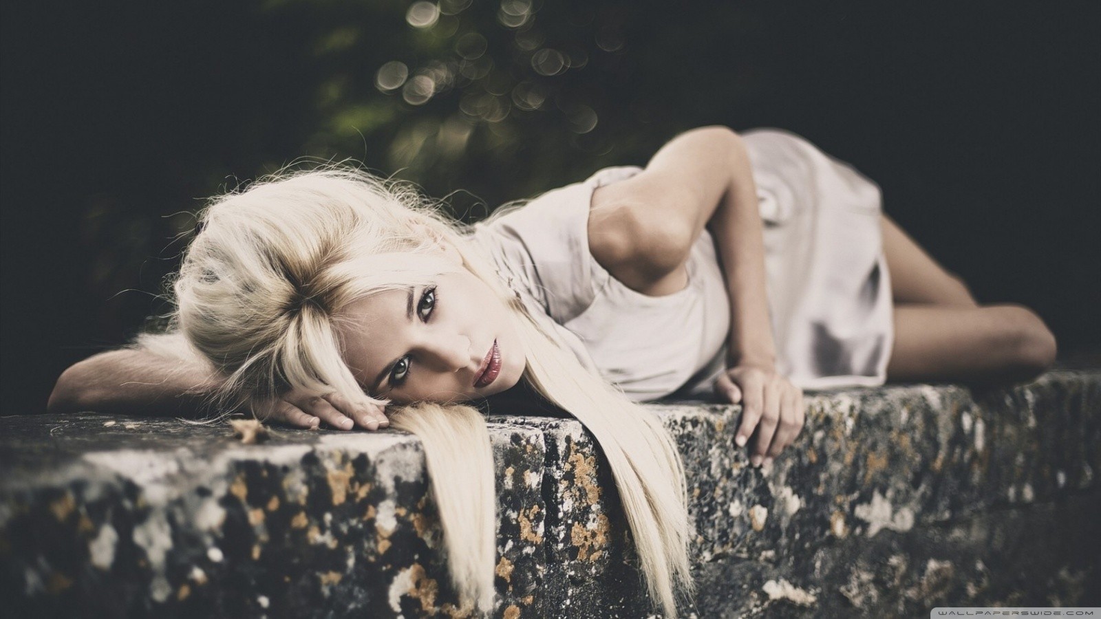 Blonde woman lying on a stone wall outdoors HD Wallpaper