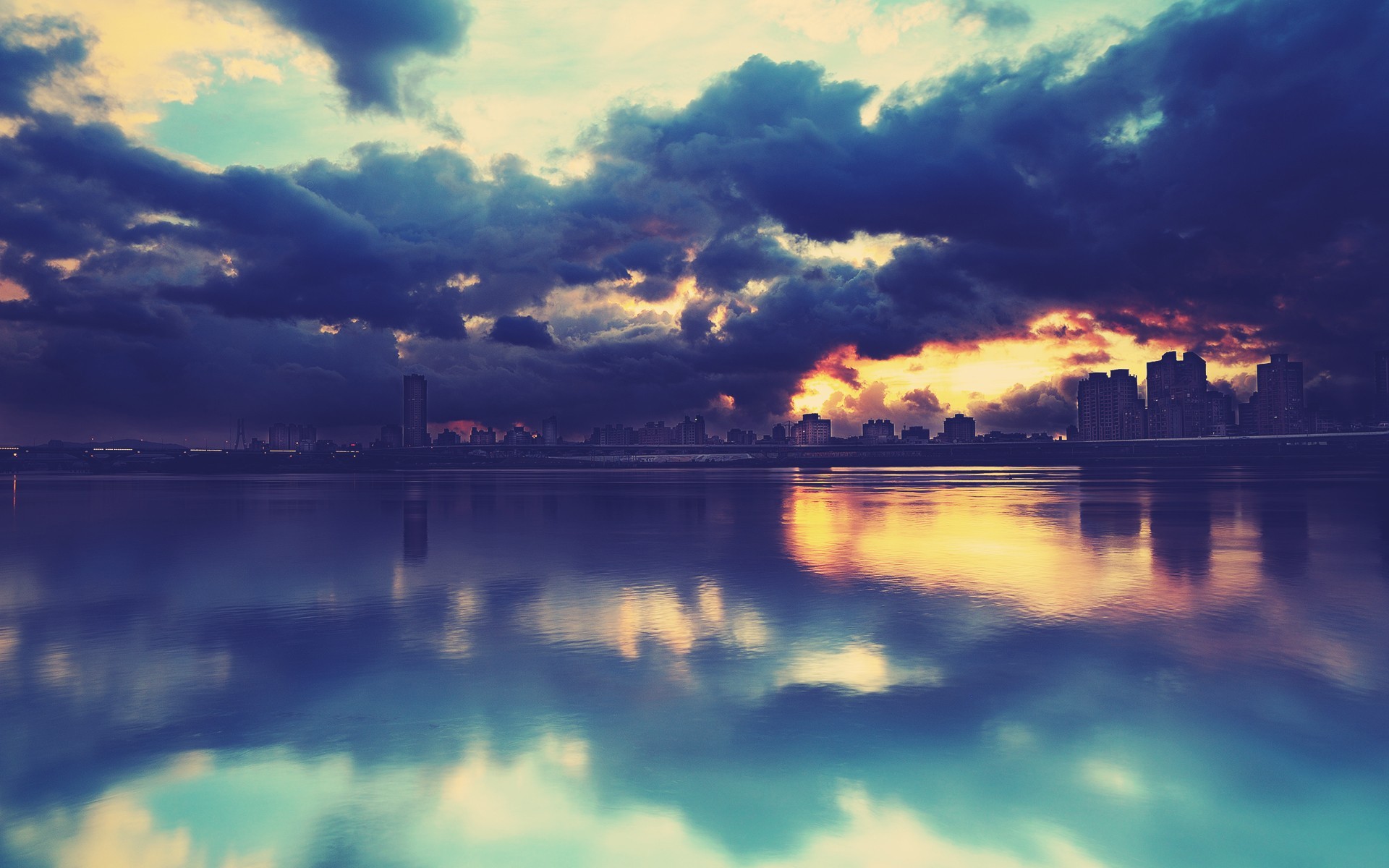 Sunset over a cityscape reflected in water HD Wallpaper