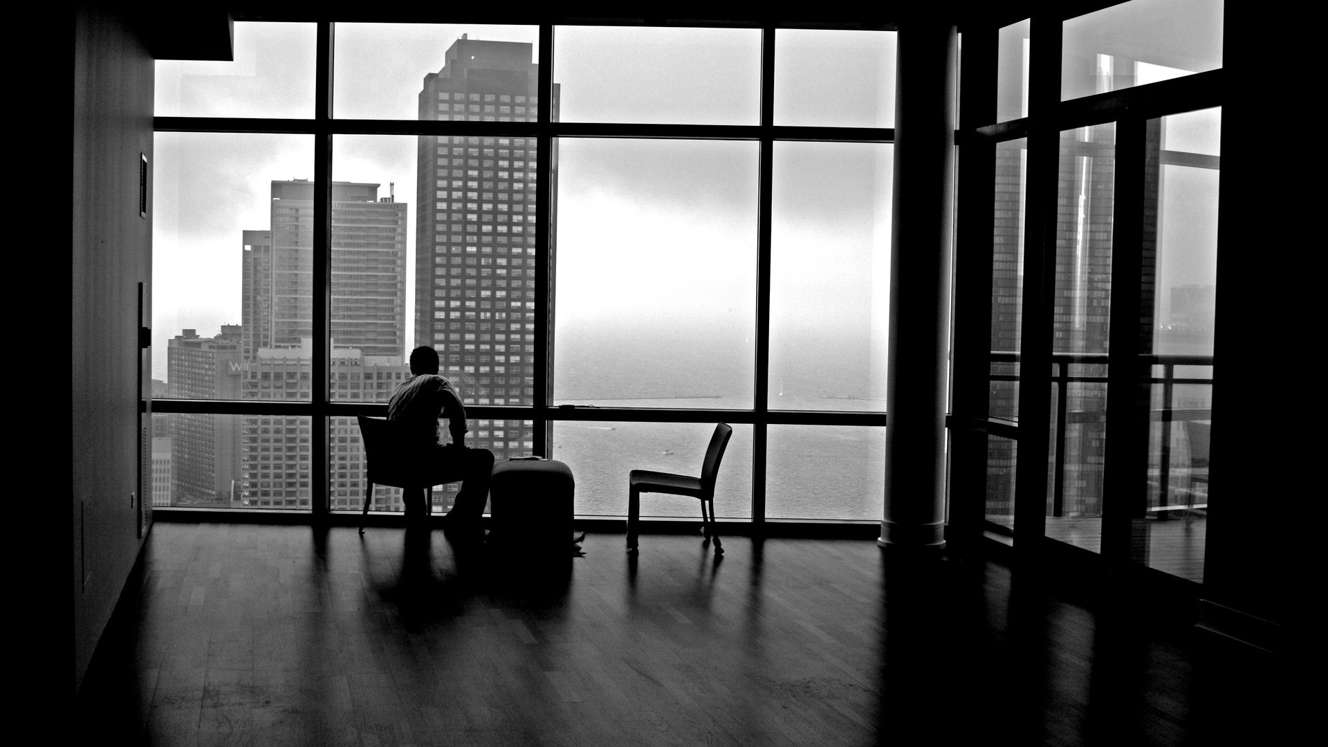 Man sitting by a large window overlooking a cityscape HD Wallpaper