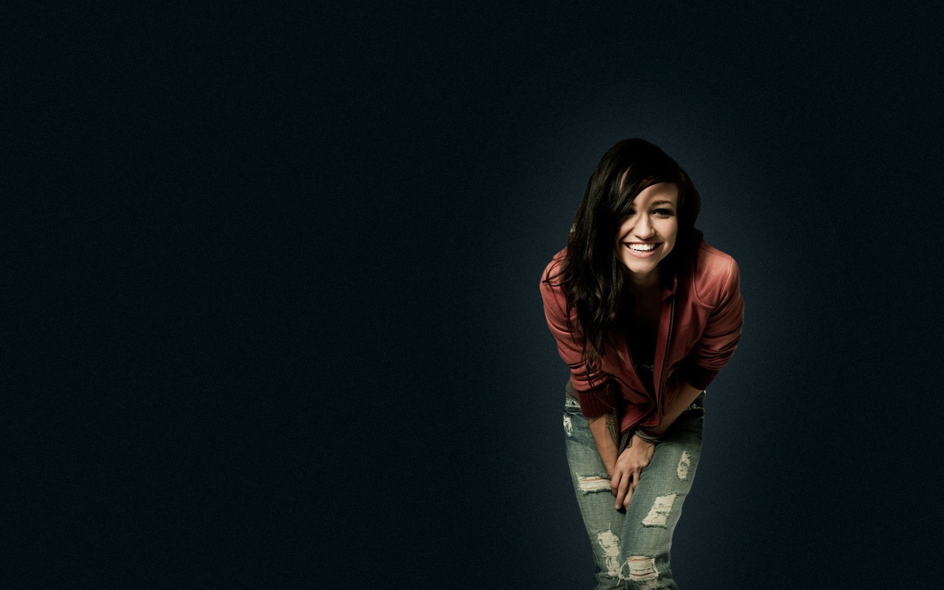 Woman in pink jacket and ripped jeans smiling HD Wallpaper