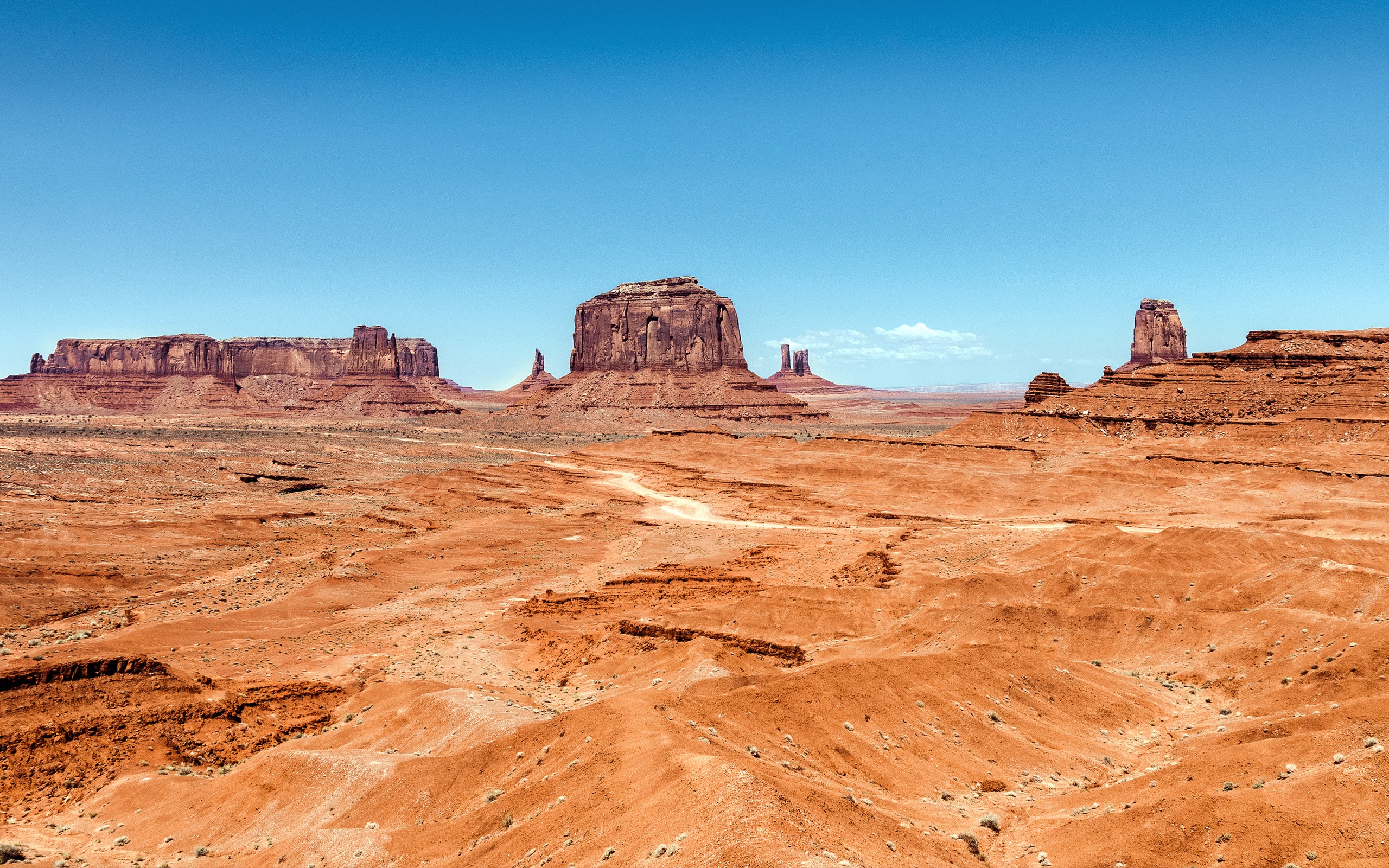 Monument Valley desert landscape with mesas under a blue sky HD Wallpaper