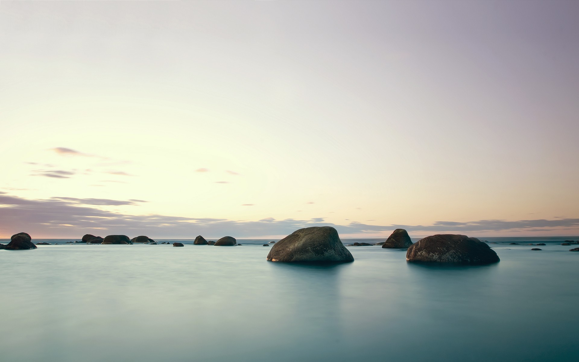 Large rocks in the ocean under a pale sky HD Wallpaper