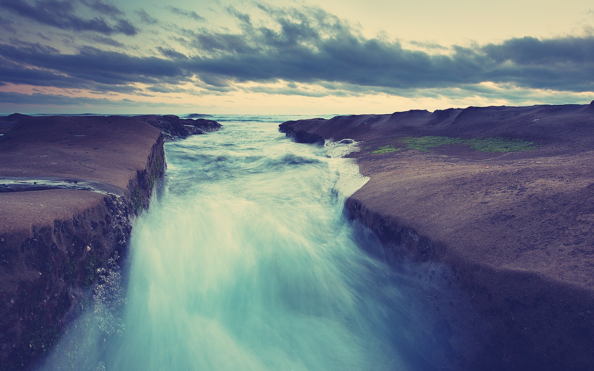 Ocean waves crashing on rocky shore under cloudy sky HD Wallpaper