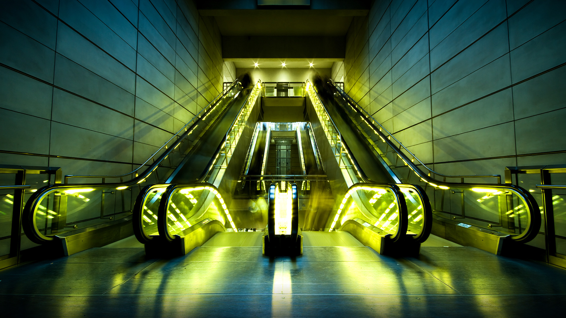 Modern escalators with yellow lighting in a subway station HD Wallpaper