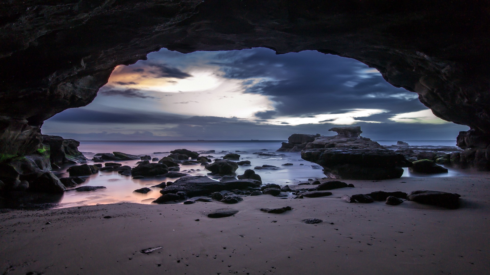 Cave entrance overlooking a rocky beach at dusk HD Wallpaper