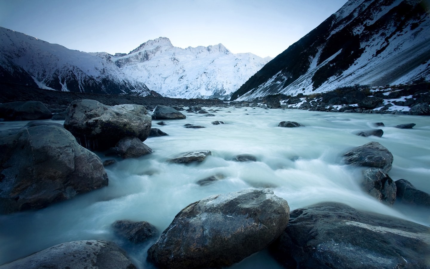 River flowing through a rocky valley with snow-capped mountains HD Wallpaper
