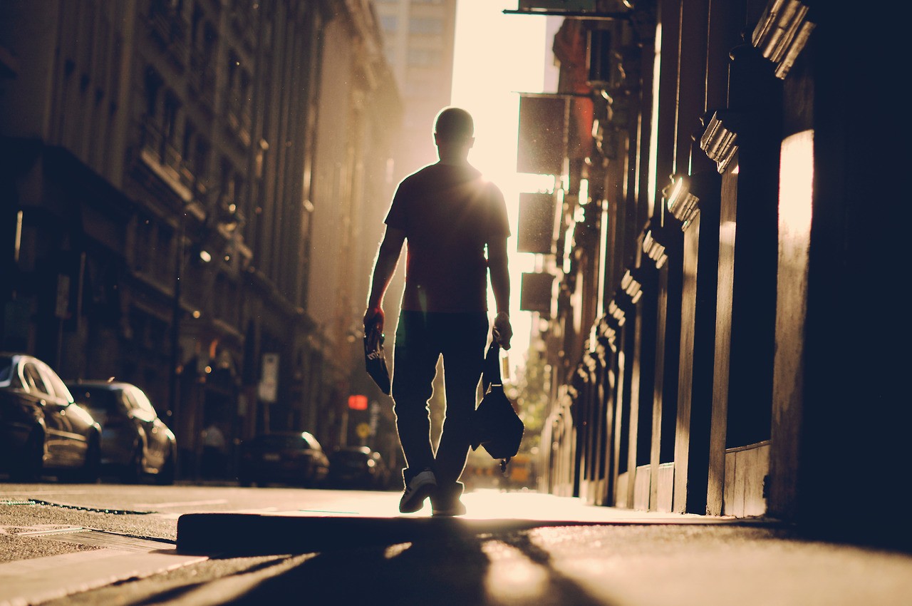 Man walking down a sunlit city street HD Wallpaper