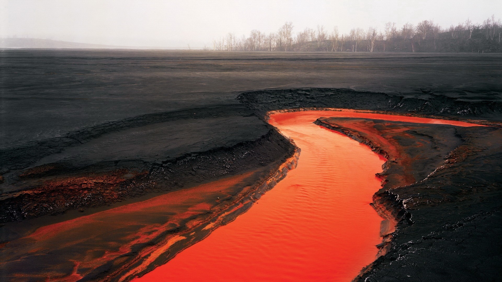 Orange river flowing through black volcanic landscape HD Wallpaper