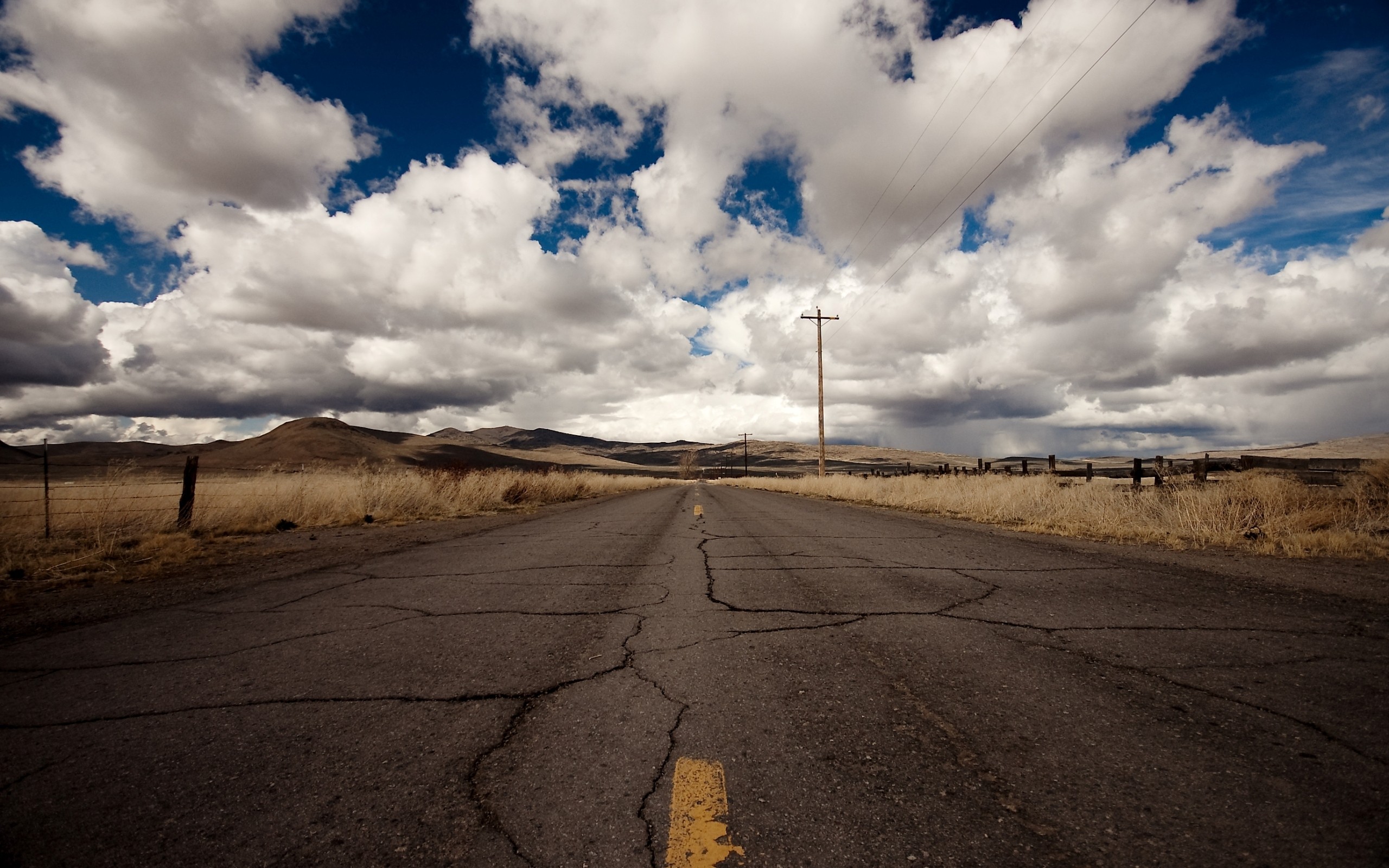 Cracked asphalt road through a dry landscape under cloudy sky HD Wallpaper