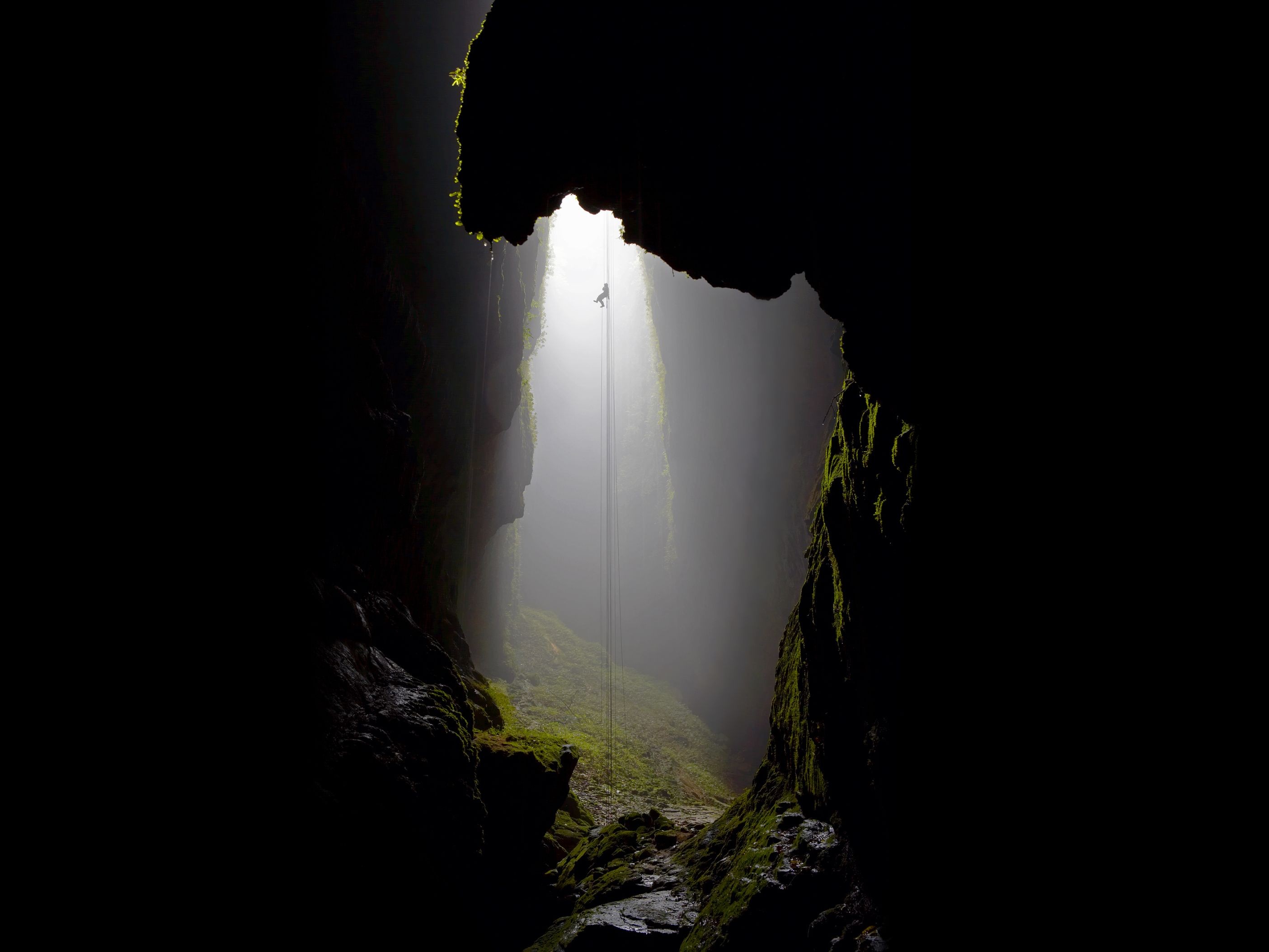 Spelunker rappelling down into a misty cave opening HD Wallpaper
