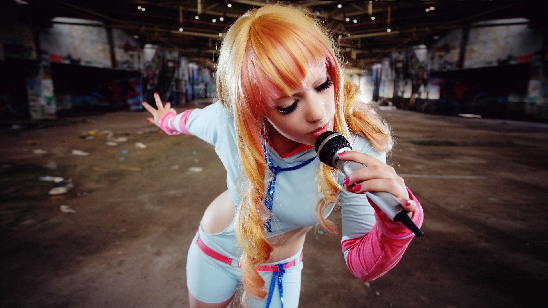 Woman with dyed hair singing into a microphone in a hangar HD Wallpaper