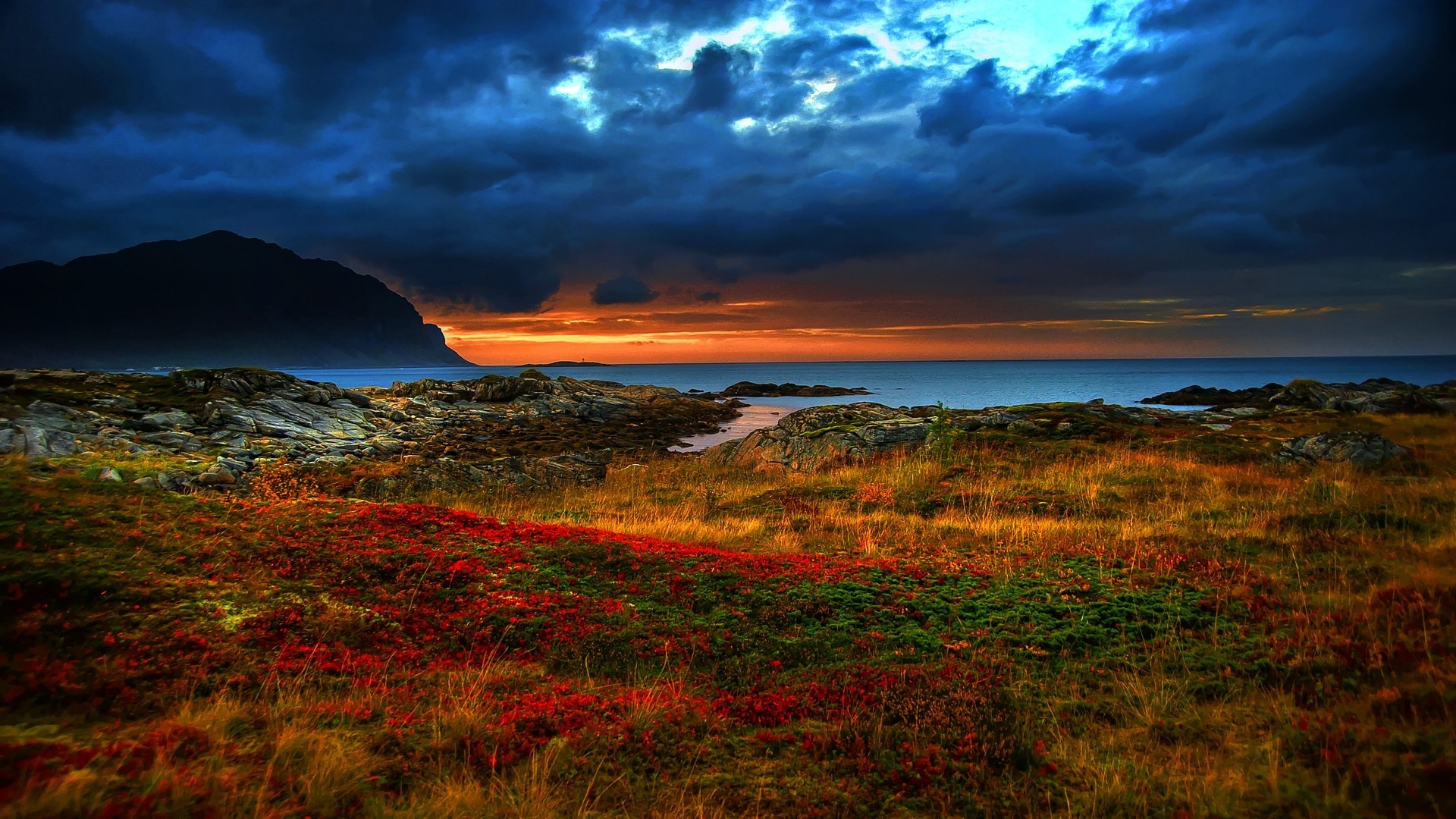 Dramatic sunset over a rocky coastline with stormy clouds HD Wallpaper