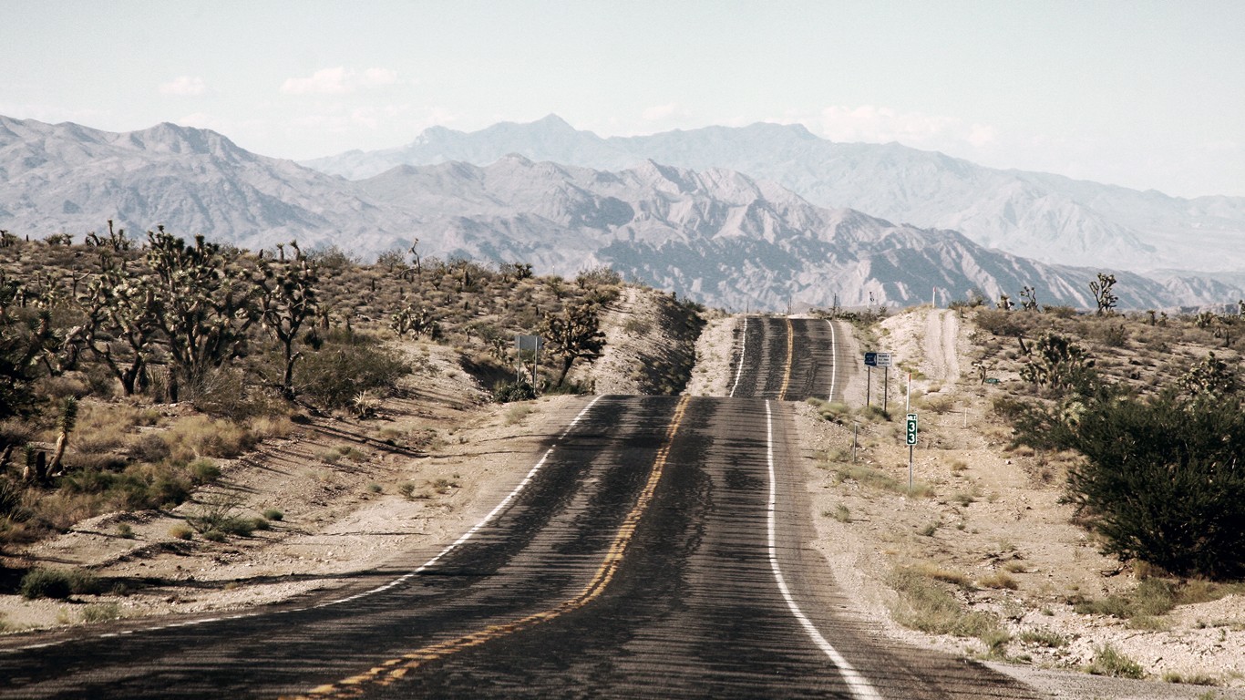 Desert road leading to mountains with Joshua trees HD Wallpaper