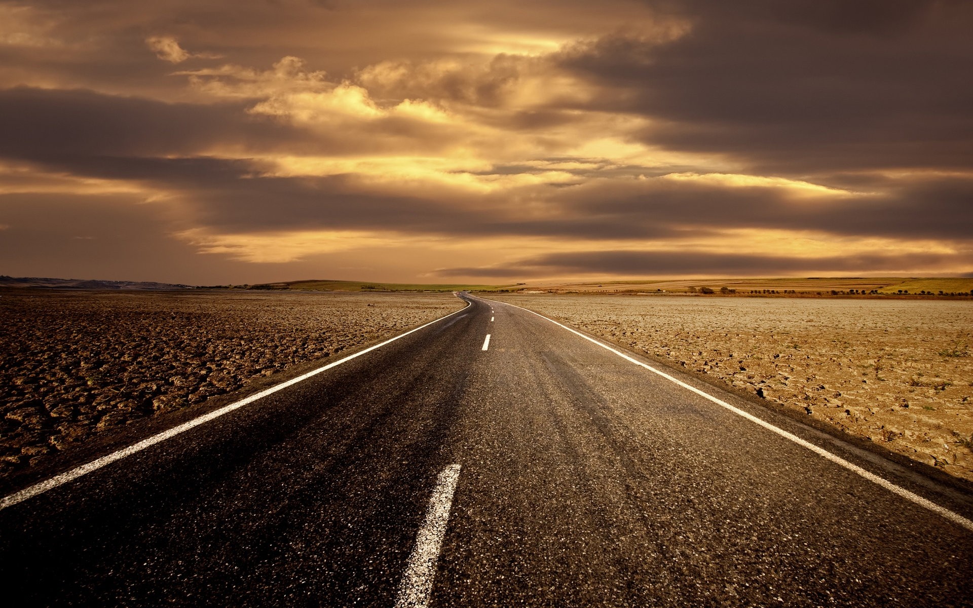 A lonely road through a dry landscape under dramatic clouds HD Wallpaper