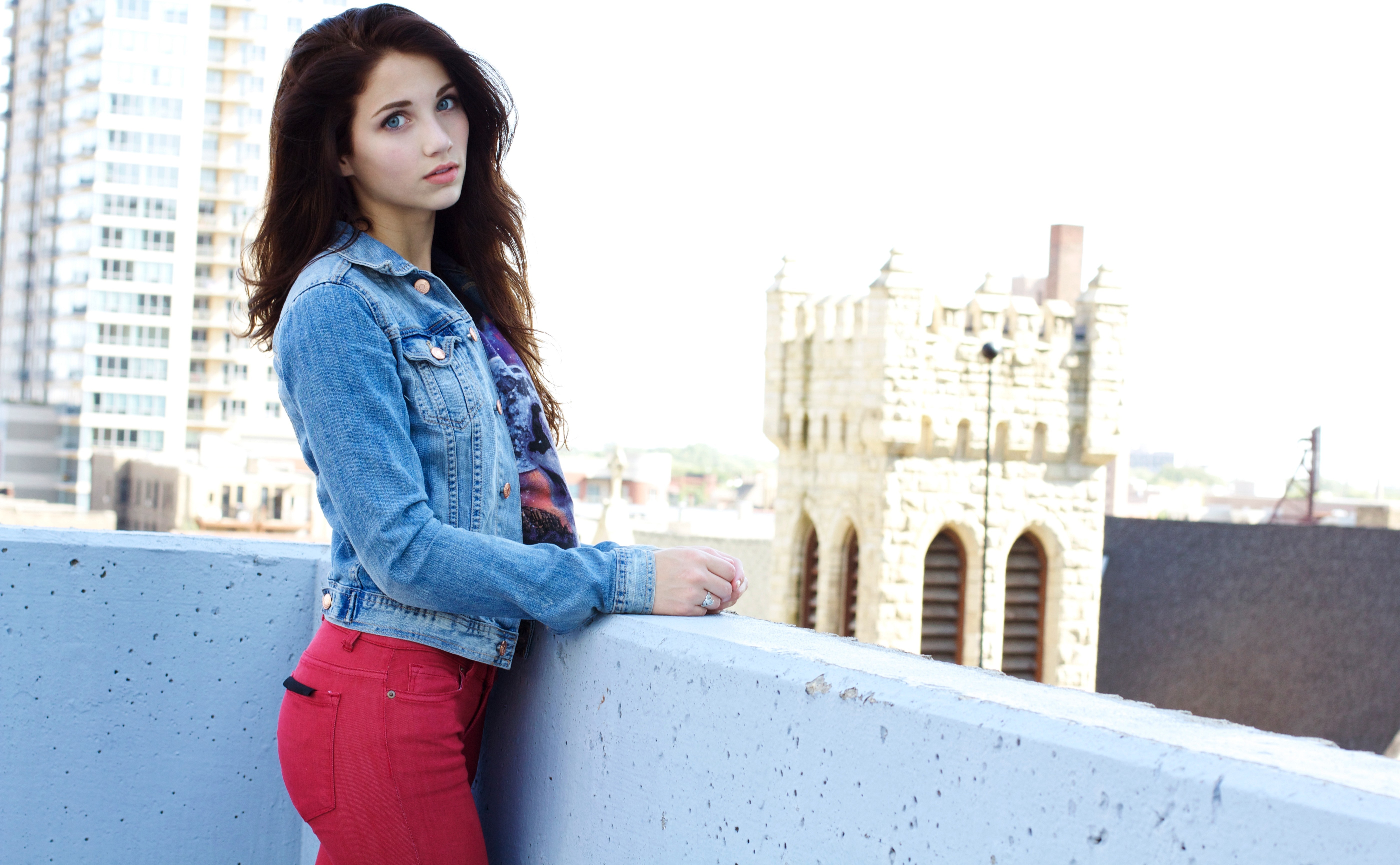 Emily Rudd on a rooftop with buildings and a tower HD Wallpaper