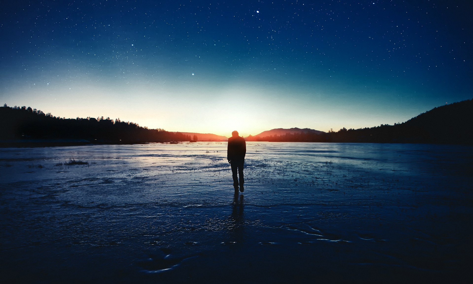 Man standing on frozen lake under starry sky at sunset HD Wallpaper