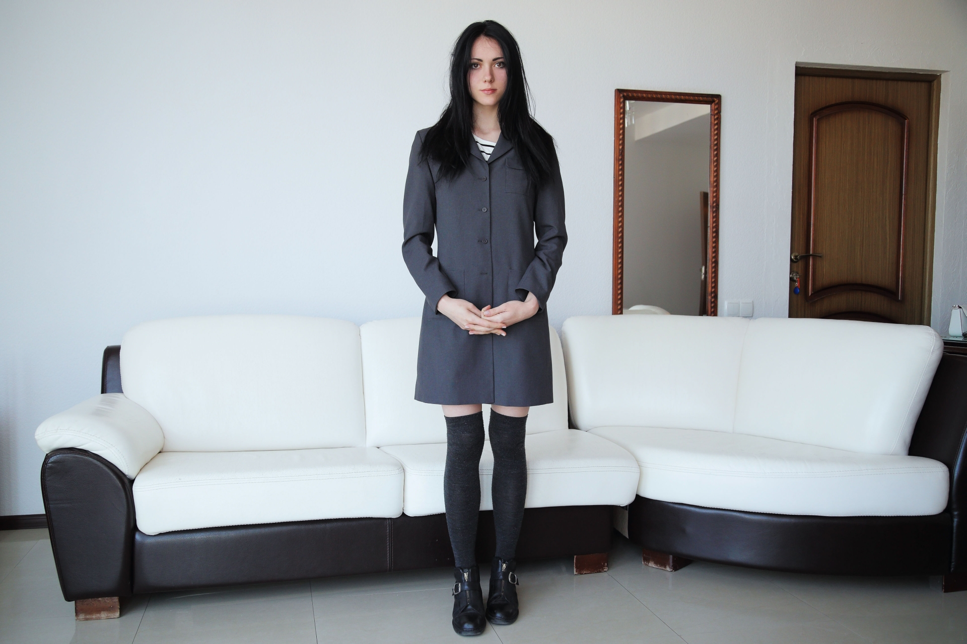 Woman in a gray coat and knee-highs standing by a couch HD Wallpaper