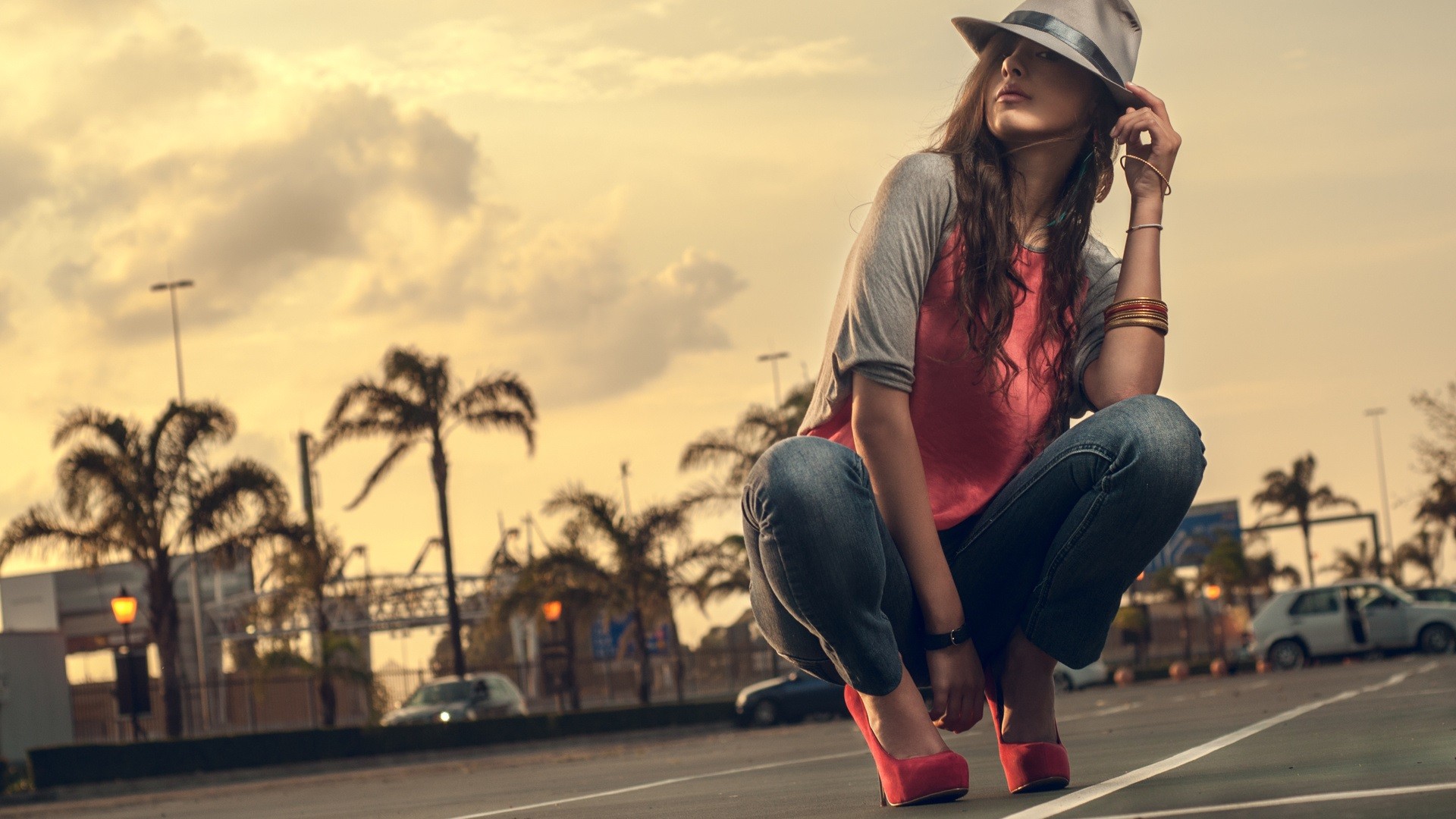 Woman in hat and jeans crouching outdoors HD Wallpaper