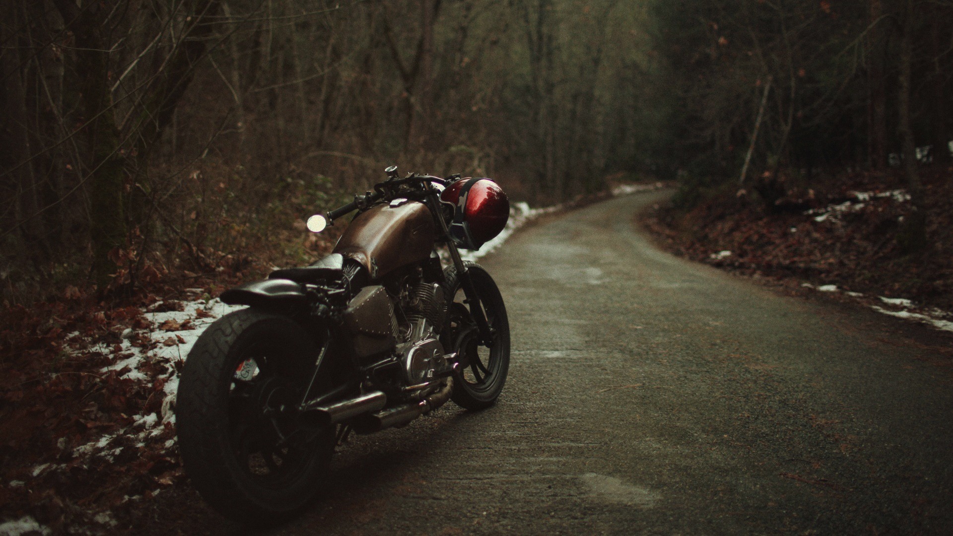 Motorcycle parked on a winding road in a forest HD Wallpaper
