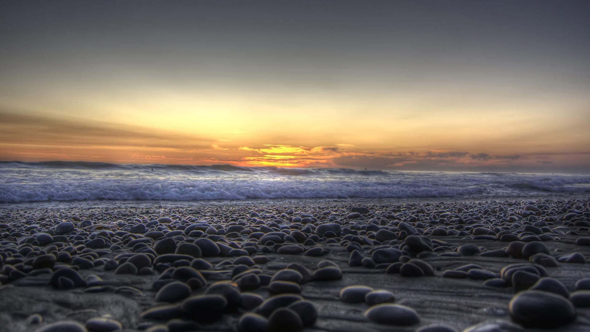 Pebble beach at sunset with ocean waves HD Wallpaper