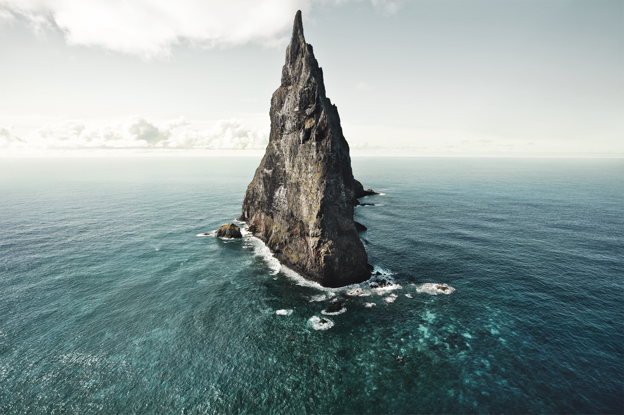 A tall rock formation in the middle of the sea HD Wallpaper