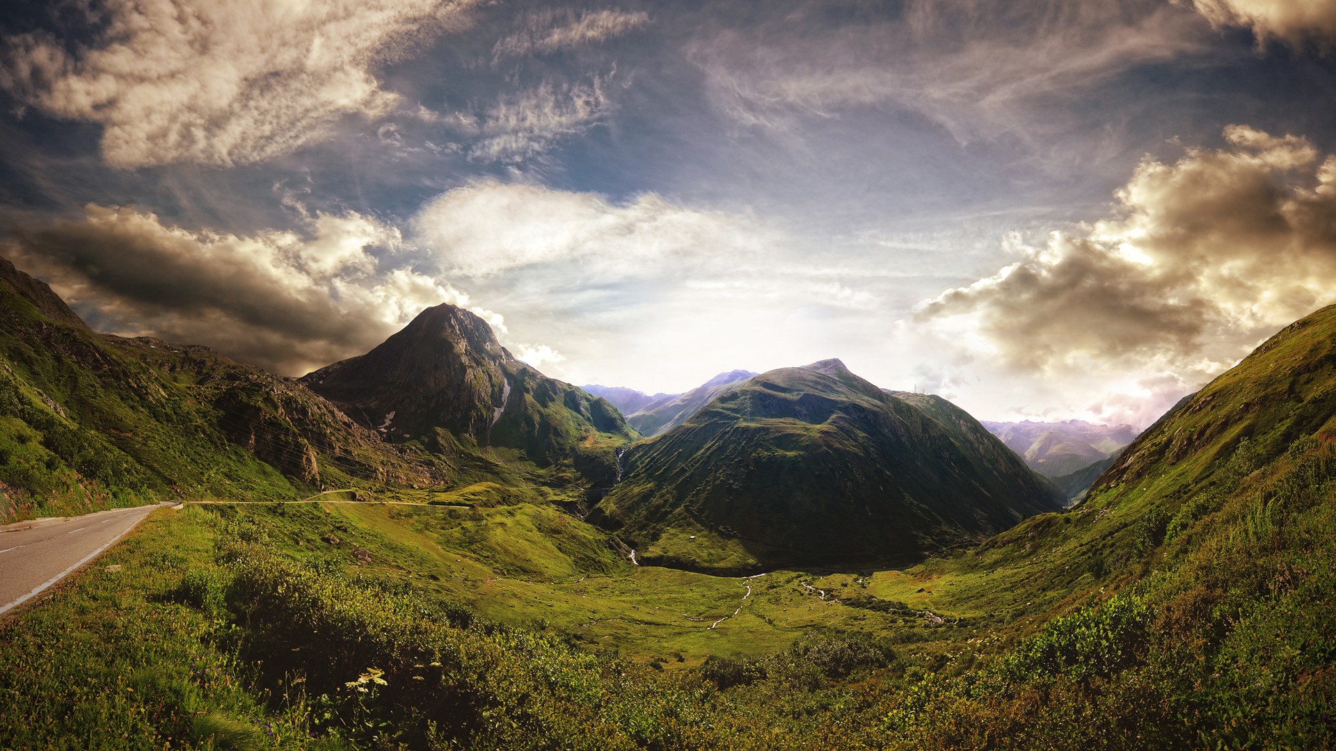 Mountain valley with a road and dramatic clouds HD Wallpaper