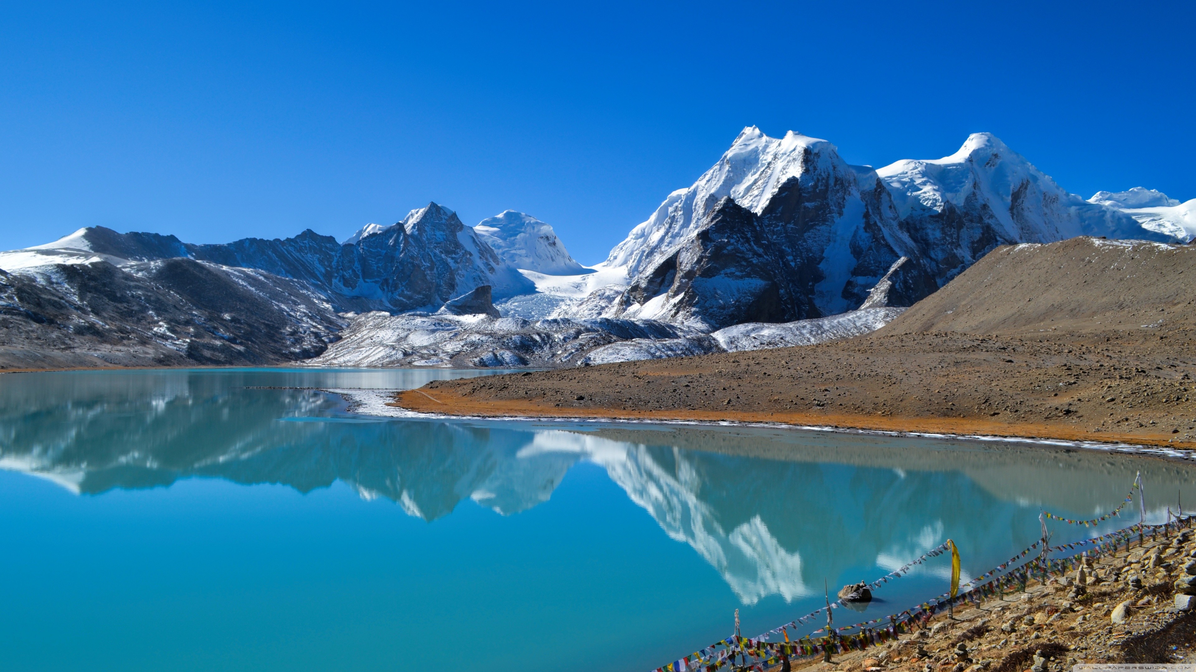 Turquoise lake reflecting snow-capped mountains under a clear blue sky HD Wallpaper