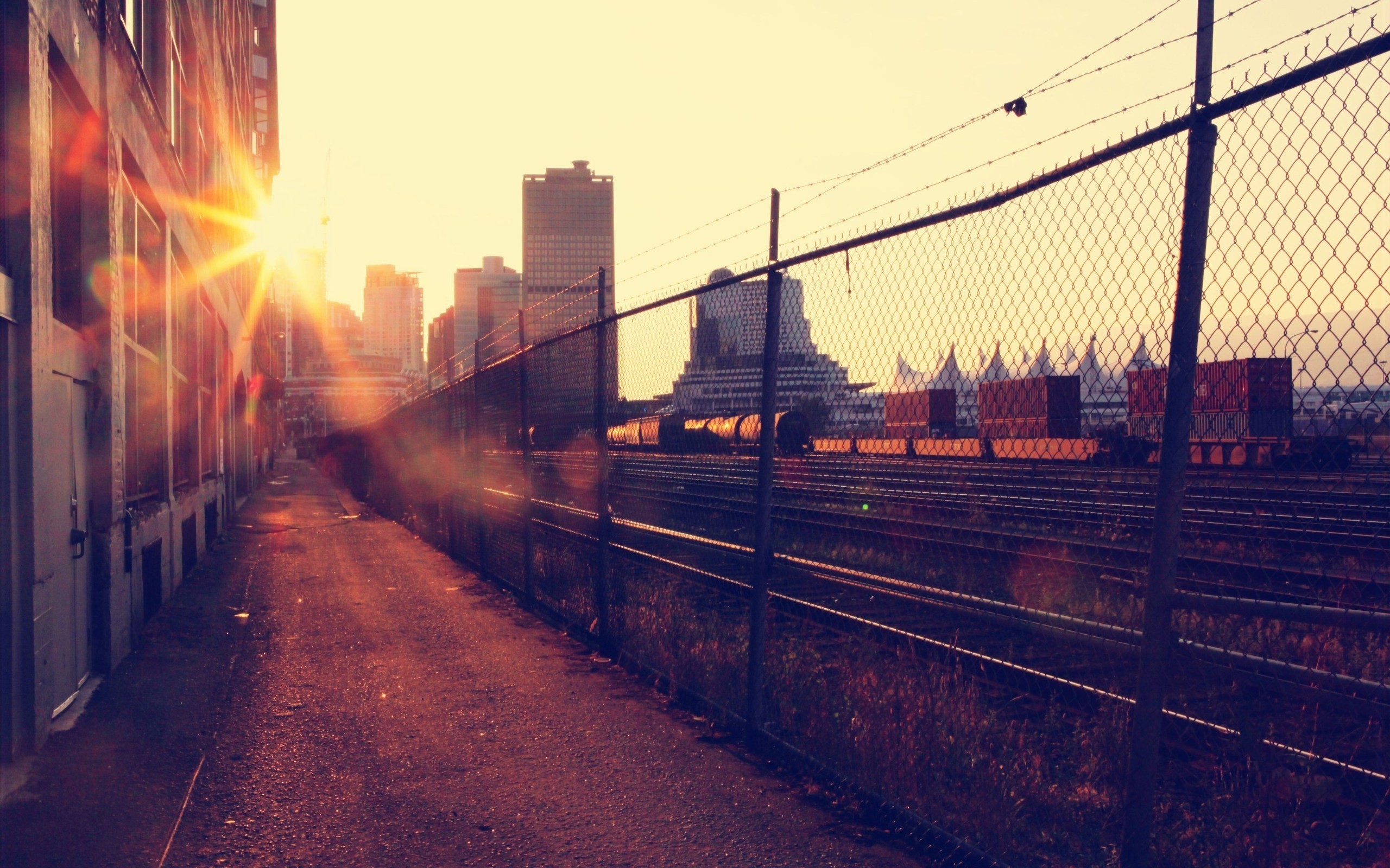 Urban cityscape with train tracks and a fence at sunset HD Wallpaper