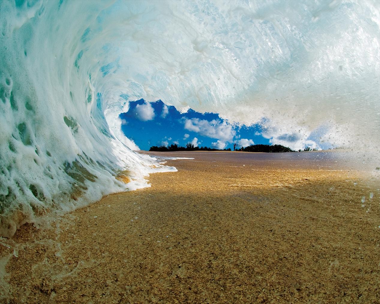 Wave crashing on a sandy beach with blue sky HD Wallpaper