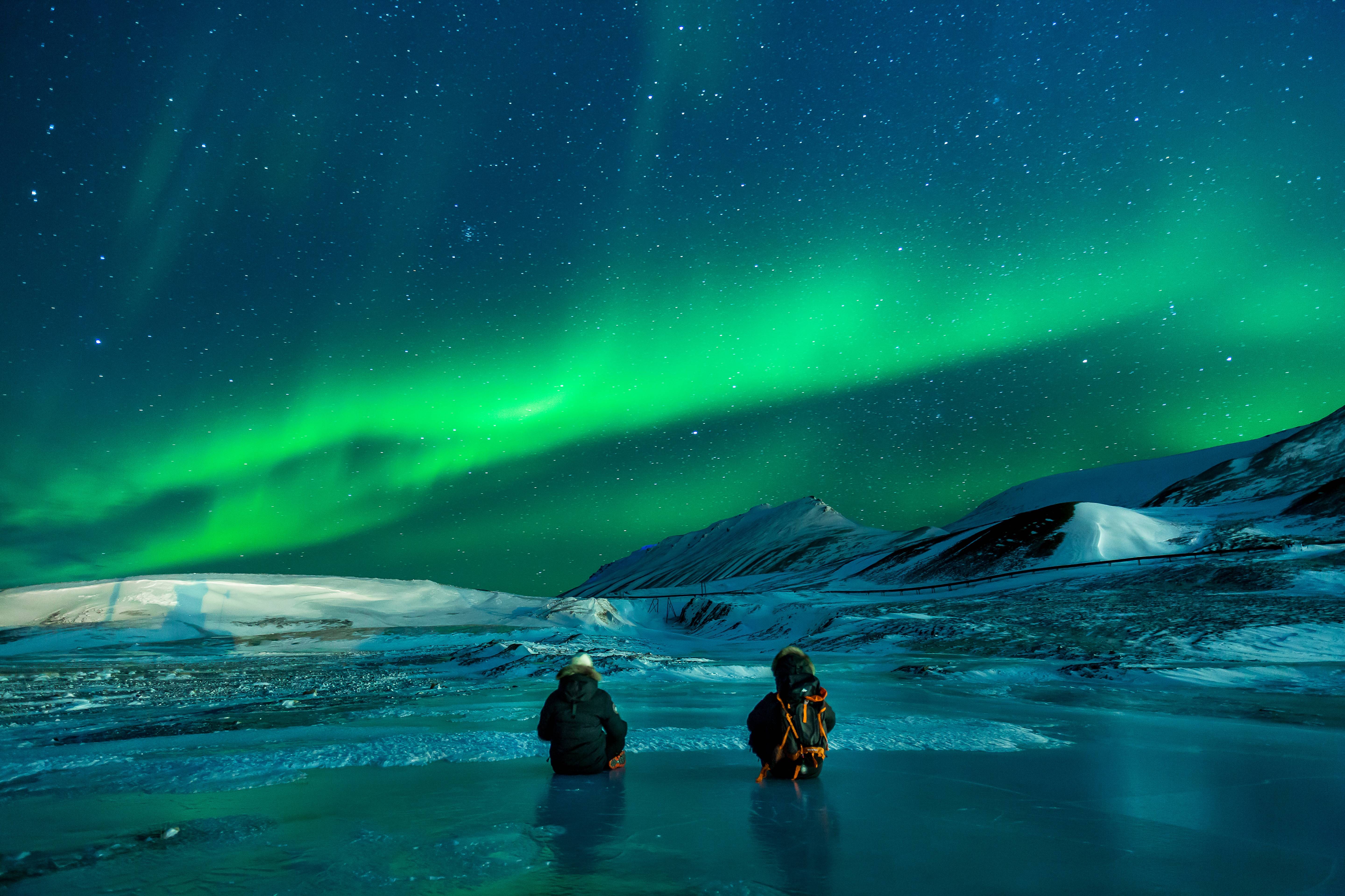People watch the Aurora Borealis over a snowy landscape HD Wallpaper