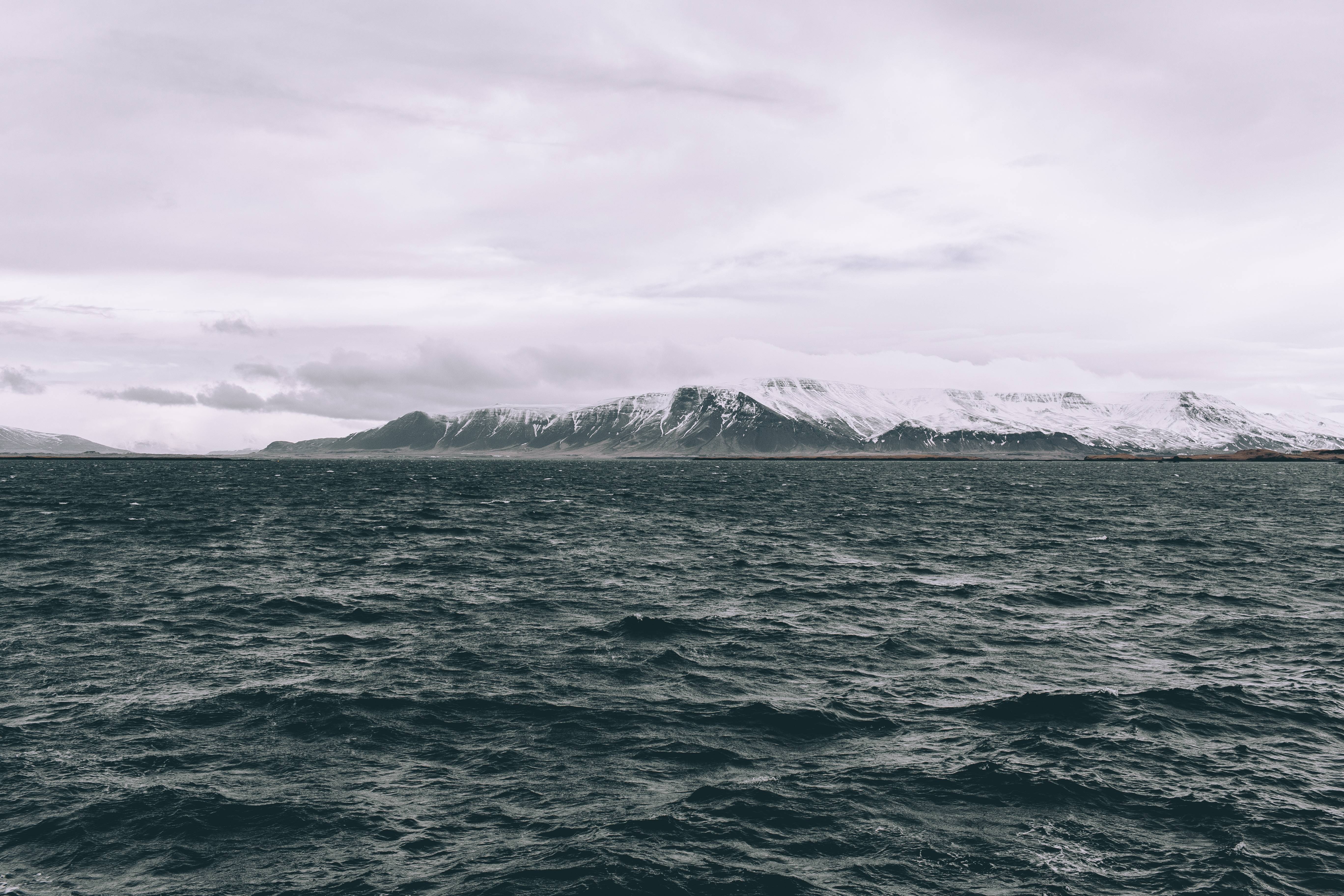 Ocean and snow-capped mountains under a cloudy sky HD Wallpaper