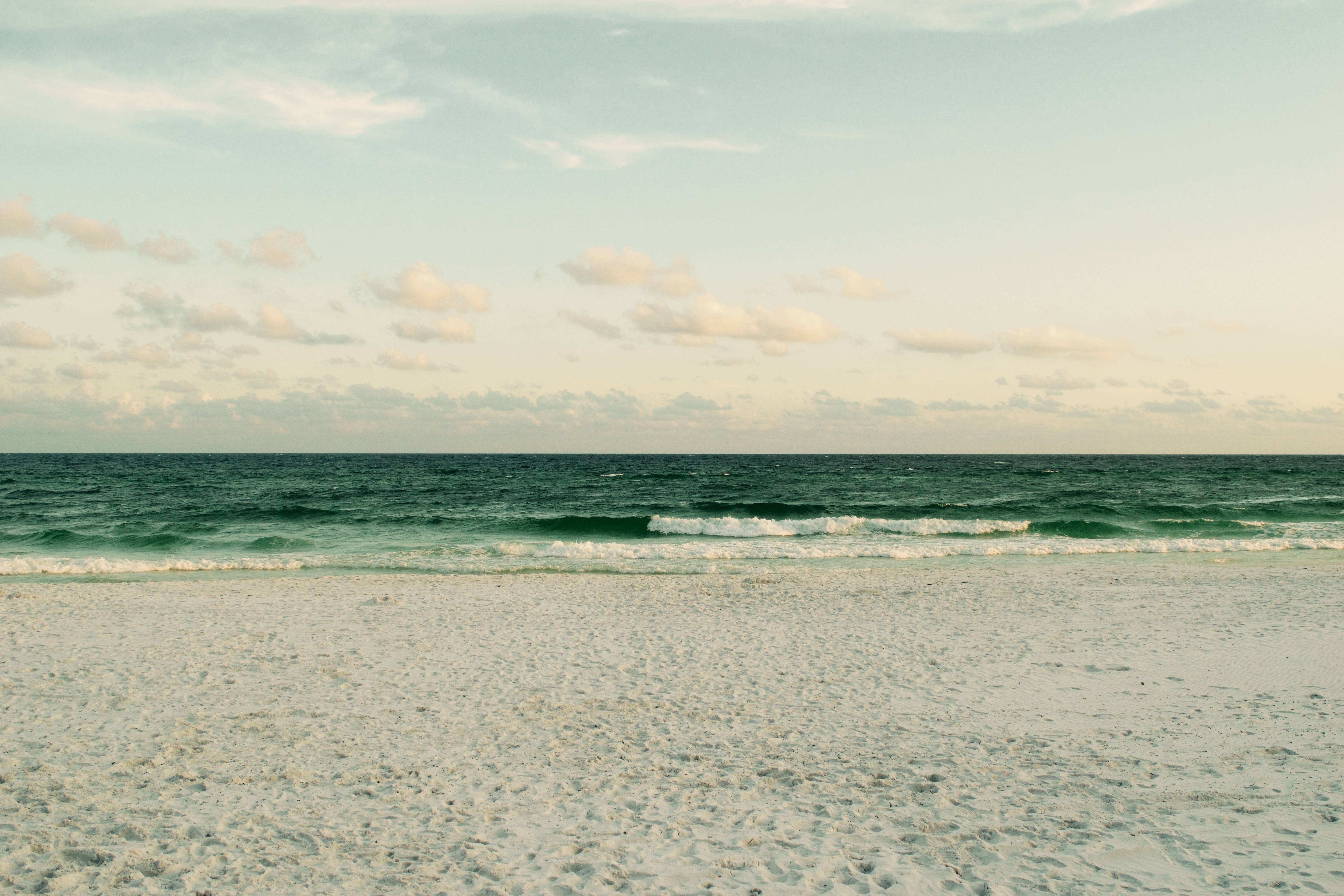 Ocean waves on a sandy beach under a cloudy sky HD Wallpaper
