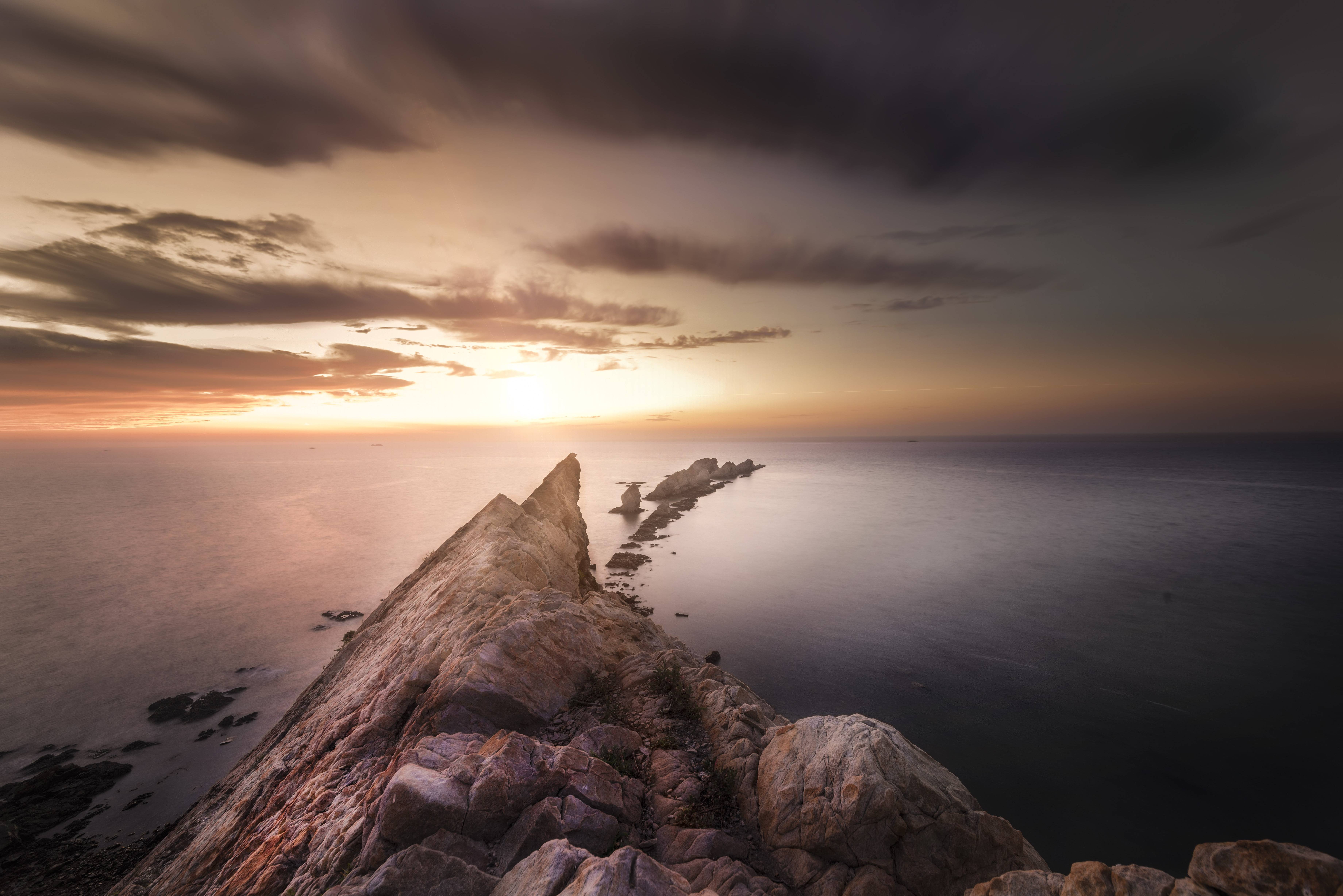 Rocky coastline at sunset over the ocean HD Wallpaper